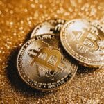 Close-up of shiny bitcoins on a gold glitter background, symbolizing cryptocurrency wealth.
