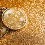 A close-up image of bitcoins placed on a sparkling gold glitter background, symbolizing cryptocurrency wealth.