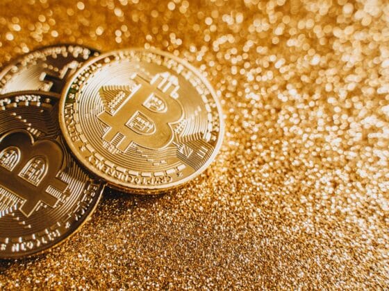 A close-up image of bitcoins placed on a sparkling gold glitter background, symbolizing cryptocurrency wealth.