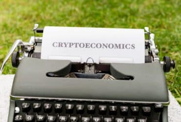 An antique typewriter with cryptoeconomics text on paper against a grassy background.