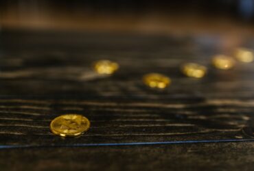Close-up of multiple gold Bitcoin coins on a wooden table, representing wealth and cryptocurrency.