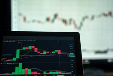 A laptop displays a detailed cryptocurrency trading chart with candlestick patterns.
