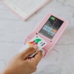 Hand using a contactless card on a pink POS terminal for a wireless transaction.
