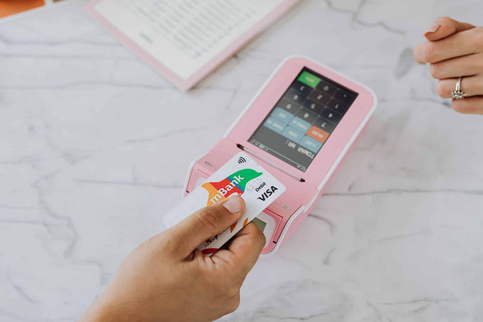 Hand using a contactless card on a pink POS terminal for a wireless transaction.