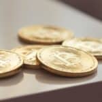 Close-up of shiny gold Bitcoin coins on white surface, symbolizing cryptocurrency wealth.