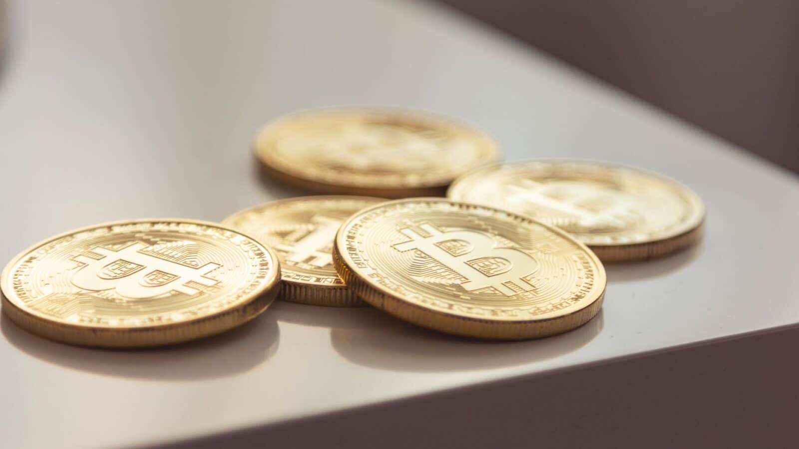 Close-up of shiny gold Bitcoin coins on white surface, symbolizing cryptocurrency wealth.