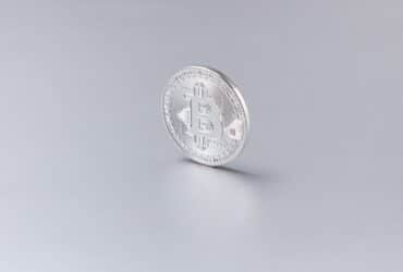 Close-up of a silver Bitcoin coin standing upright against a clean, white background.