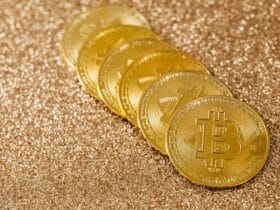 A stack of gold Bitcoin coins placed on a shimmering gold glitter background.