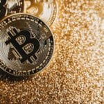 Close-up view of shining Bitcoin coins on a glittering golden background representing digital wealth.