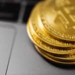 Stack of gold Bitcoin coins on a laptop keyboard, symbolizing digital currency technology and wealth.