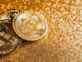 A close-up image of bitcoins placed on a sparkling gold glitter background, symbolizing cryptocurrency wealth.