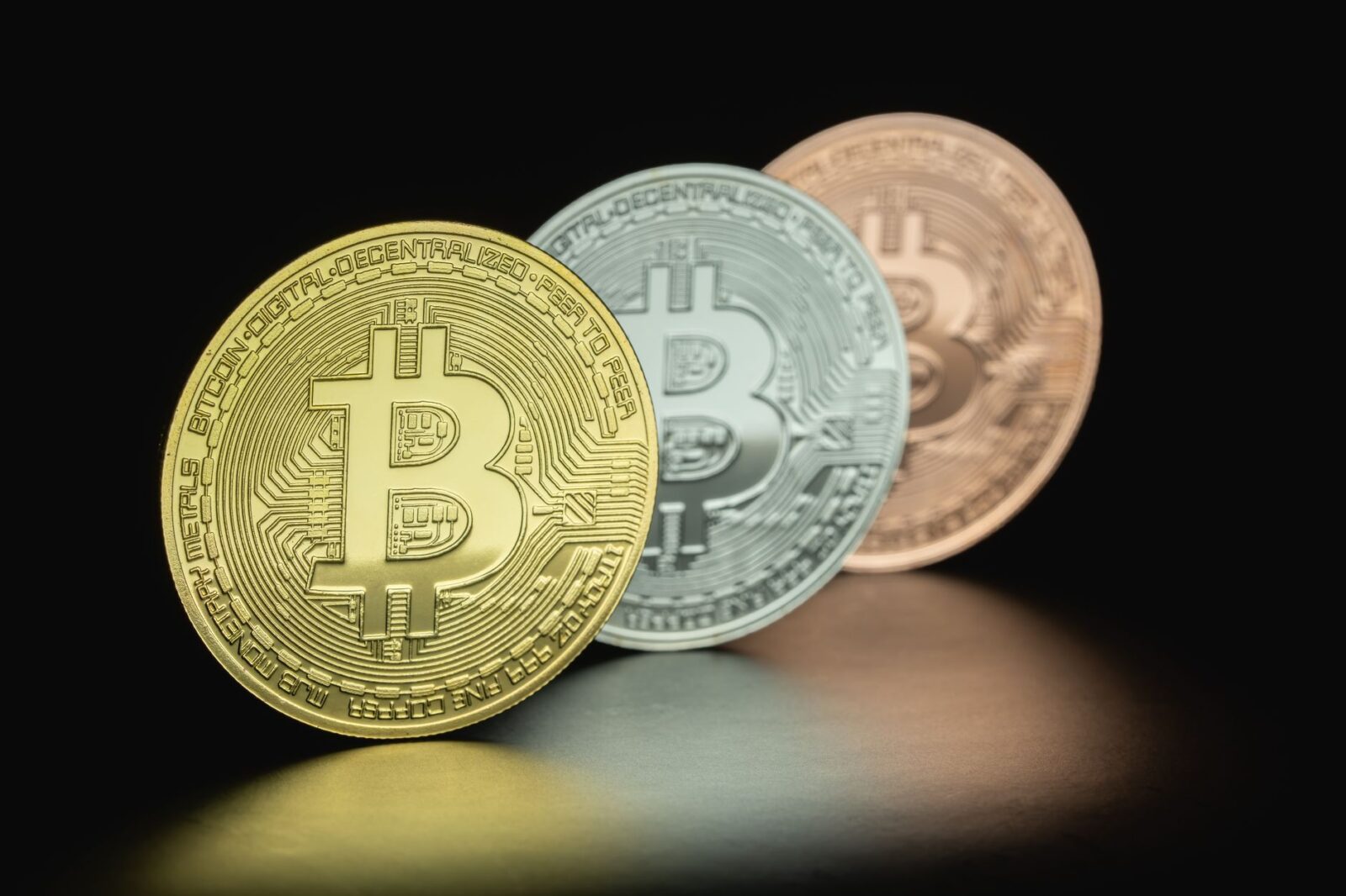 Close-up image of three Bitcoin coins in gold, silver, and bronze tones against a dark background.