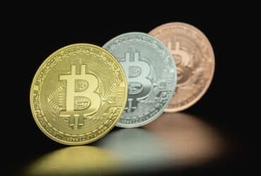 Close-up image of three Bitcoin coins in gold, silver, and bronze tones against a dark background.