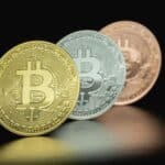 Close-up image of three Bitcoin coins in gold, silver, and bronze tones against a dark background.