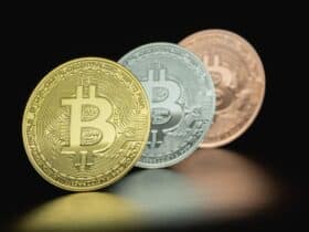 Close-up image of three Bitcoin coins in gold, silver, and bronze tones against a dark background.