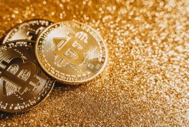 A close-up image of bitcoins placed on a sparkling gold glitter background, symbolizing cryptocurrency wealth.