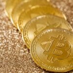 Close-up of golden Bitcoin coins on a shimmering glitter background, symbolizing digital currency's allure.