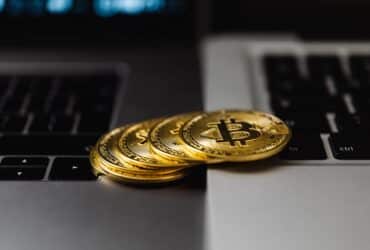 Close-up of gold Bitcoin coins placed on laptop keyboards, representing digital currency and wealth.