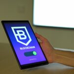 A hand holding a tablet with blockchain logo on screen, showcasing digital technology.