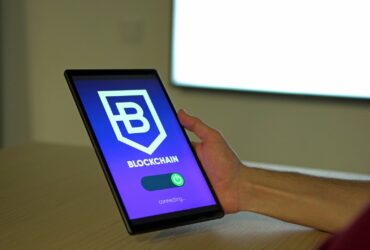 A hand holding a tablet with blockchain logo on screen, showcasing digital technology.