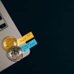 Bitcoin coins placed on a laptop keyboard with sticky note reminders about investing and checking new coins.