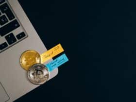 Bitcoin coins placed on a laptop keyboard with sticky note reminders about investing and checking new coins.