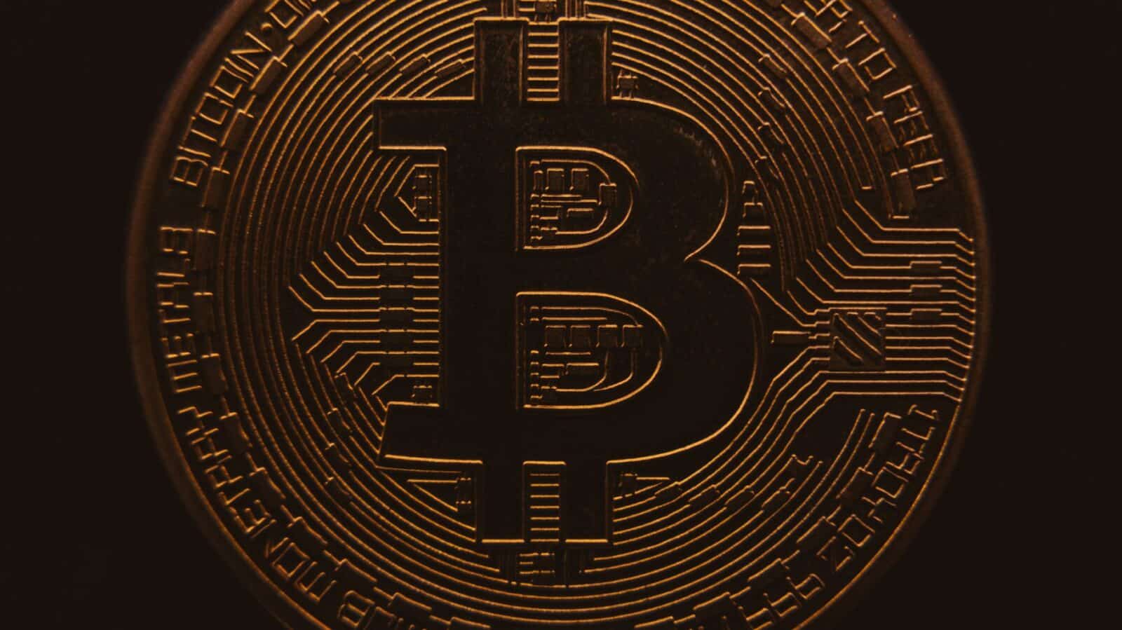 Close-up view of a bitcoin coin showing its intricate, digital design in a warm, dark ambiance.