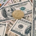 Bitcoin coin placed on scattered US dollar bills, representing cryptocurrency and finance.