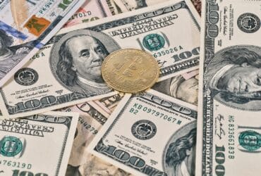 Bitcoin coin placed on scattered US dollar bills, representing cryptocurrency and finance.