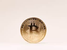 A golden Bitcoin coin standing upright against a minimalist light background.