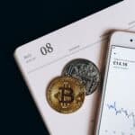 A smartphone displays cryptocurrency data alongside Bitcoin and Ethereum coins on an August calendar.
