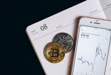 A smartphone displays cryptocurrency data alongside Bitcoin and Ethereum coins on an August calendar.