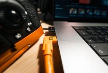 A close-up view of a camera connected to a laptop using an orange cable, highlighting studio equipment setup.