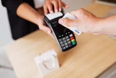 Close-up of hands using a contactless payment terminal with a credit card indoors.
