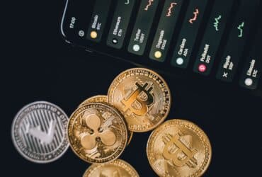 Close-up view of various cryptocurrency coins with a digital market display in the background.