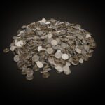 A large pile of assorted coins on a dark black background, symbolizing wealth and finance.