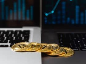 Gold bitcoins placed on laptop keyboards with digital financial graphs in the background.