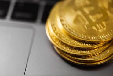 Stack of gold Bitcoin coins on a laptop keyboard, symbolizing digital currency technology and wealth.
