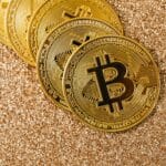 Golden Bitcoin coins arranged on a sparkling glitter surface, symbolizing cryptocurrency and wealth.