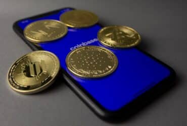 Five cryptocurrency coins displayed on a smartphone with Coinbase app open.