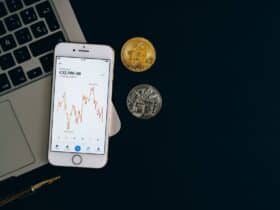 Smartphone displaying Bitcoin price chart alongside Bitcoin and Ethereum coins on black background.