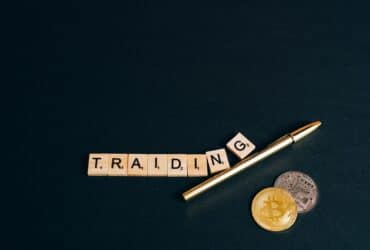Bitcoin and trading concept shown with coins, pen, and letter tiles on a dark background.