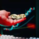 Close-up of hand holding cryptocurrency coins with trading chart in background.