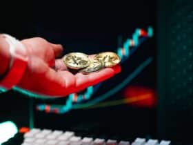 Close-up of hand holding cryptocurrency coins with trading chart in background.
