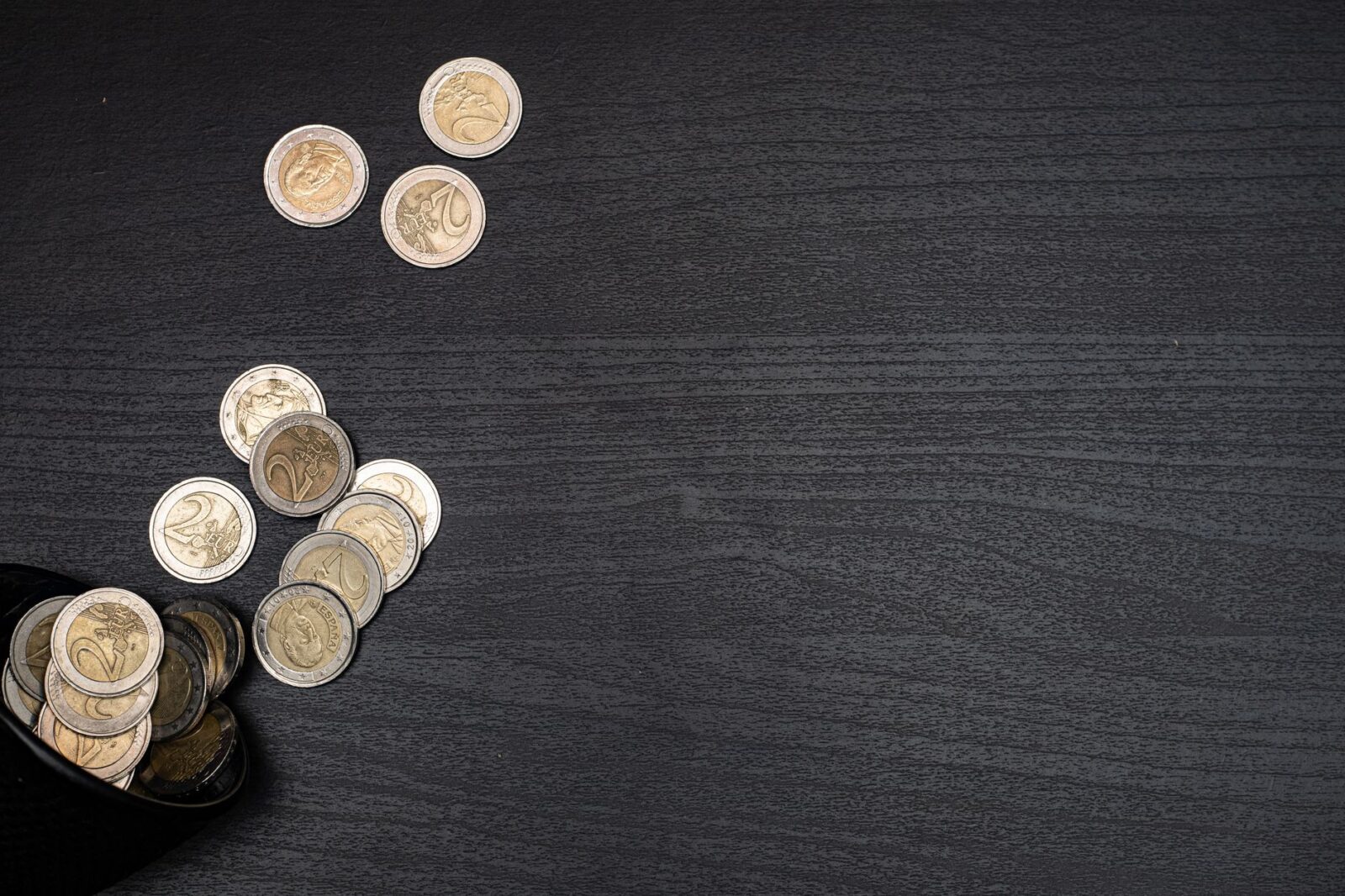 A collection of euro coins scattered on a dark textured surface, with space for text.
