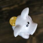 Close-up of a bitcoin coin inserted in a white piggy bank, symbolizing cryptocurrency savings.