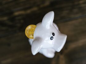 Close-up of a bitcoin coin inserted in a white piggy bank, symbolizing cryptocurrency savings.