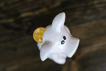 Close-up of a bitcoin coin inserted in a white piggy bank, symbolizing cryptocurrency savings.