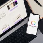 Mobile phone with Payoneer app on screen next to laptop displaying online shopping site.