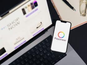 Mobile phone with Payoneer app on screen next to laptop displaying online shopping site.